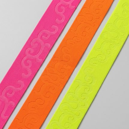Galon élastique fantaisie de 50 mm en tissage jacquard ton sur ton à motifs volutes gravées, coloris fluo vifs à forte tenue indéformable ne roulant pas, conçu pour ceintures apparentes, jupes, pantalons et customisation d'accessoires textiles.